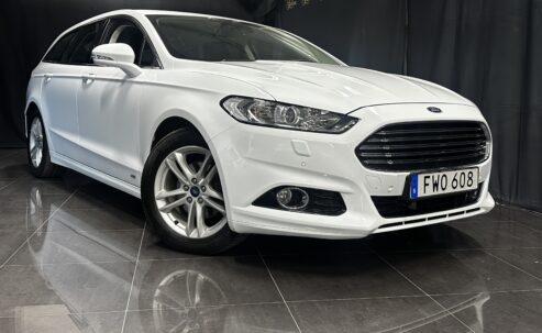 Vit Ford Mondeo Kombi 2.0 TDCi AWD Powershift, 180hk, 2019 sedan visas inomhus på ett reflekterande golv, vinklad för att visa fram och sida.